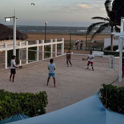 Partido de beach tennis en la cancha de la posada, con el mar al fondo.