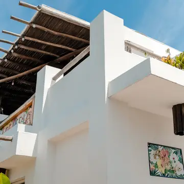 Fachada blanca de la posada con balcón y cielo azul.