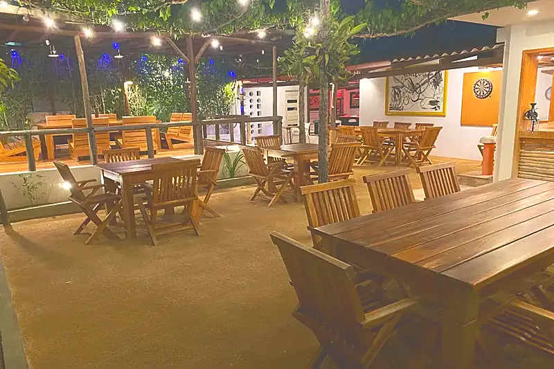 El restaurante en el jardín de noche, con luces colgantes sobre las mesas de madera.